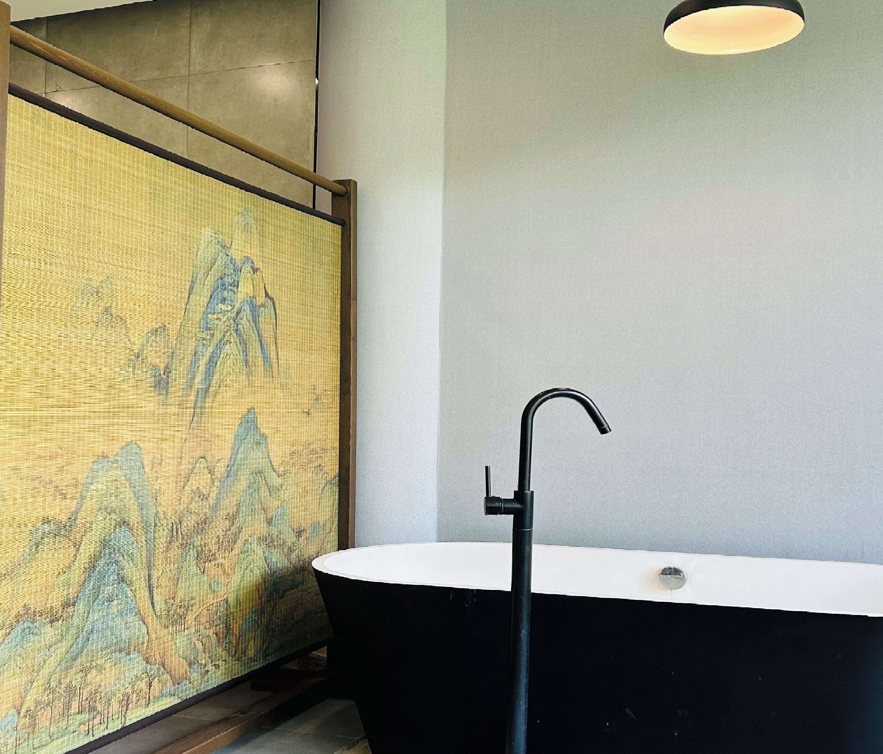 A bathroom with a black freestanding bathtub, a white sink, and a textured wall with a landscape painting.