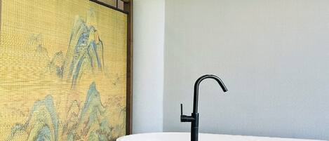 Un baño con una bañera independiente negra, un lavabo blanco y una pared texturizada con un cuadro de paisaje.
