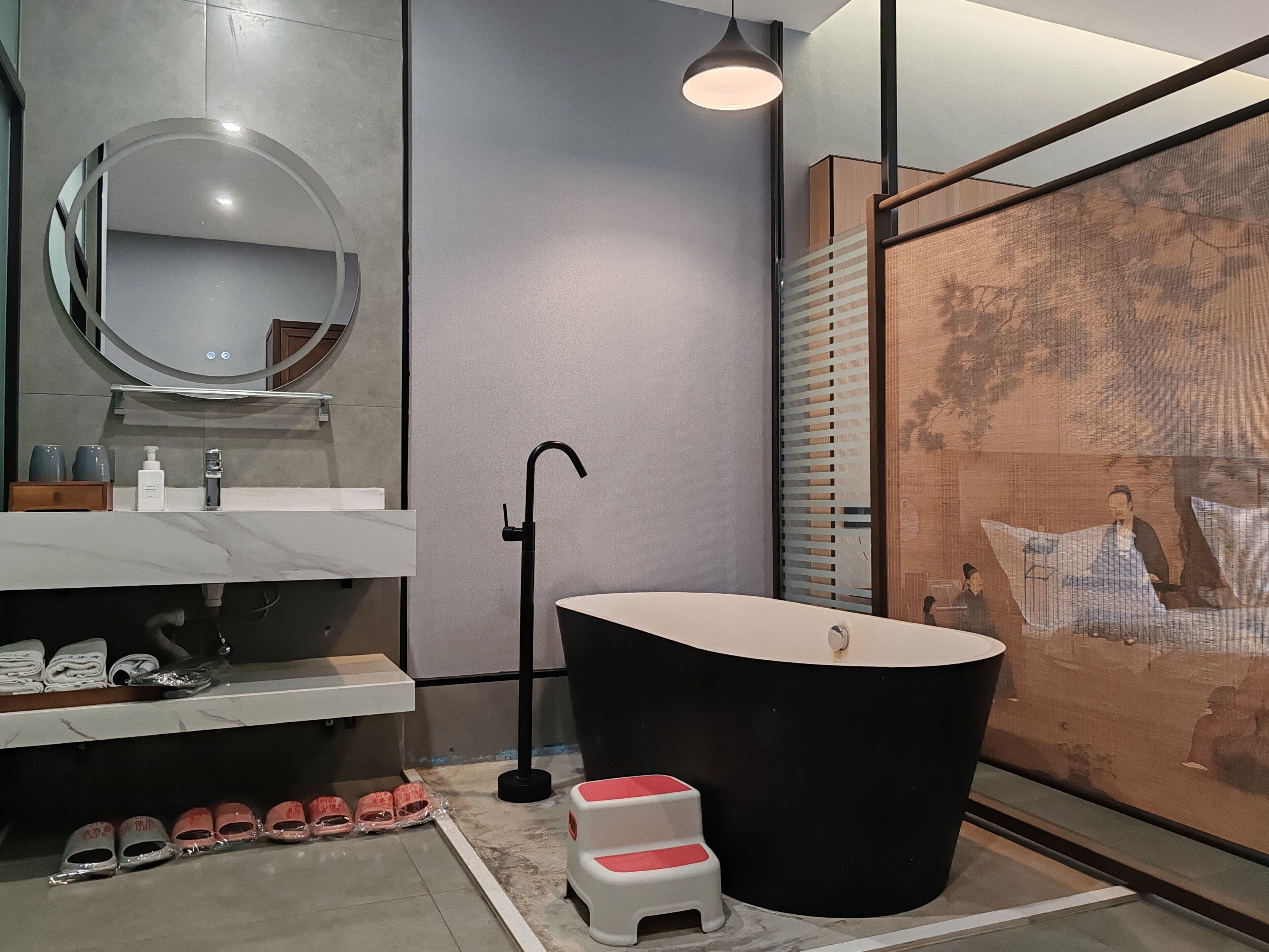 Un baño moderno con una bañera grande, un espejo redondo, un lavabo con artículos de aseo y un taburete pequeño.