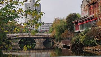 Een traditioneel gebouw met een pannendak en rode lantaarns, een stenen brug over een rustige rivier, en moderne wolkenkrabbers op de achtergrond.