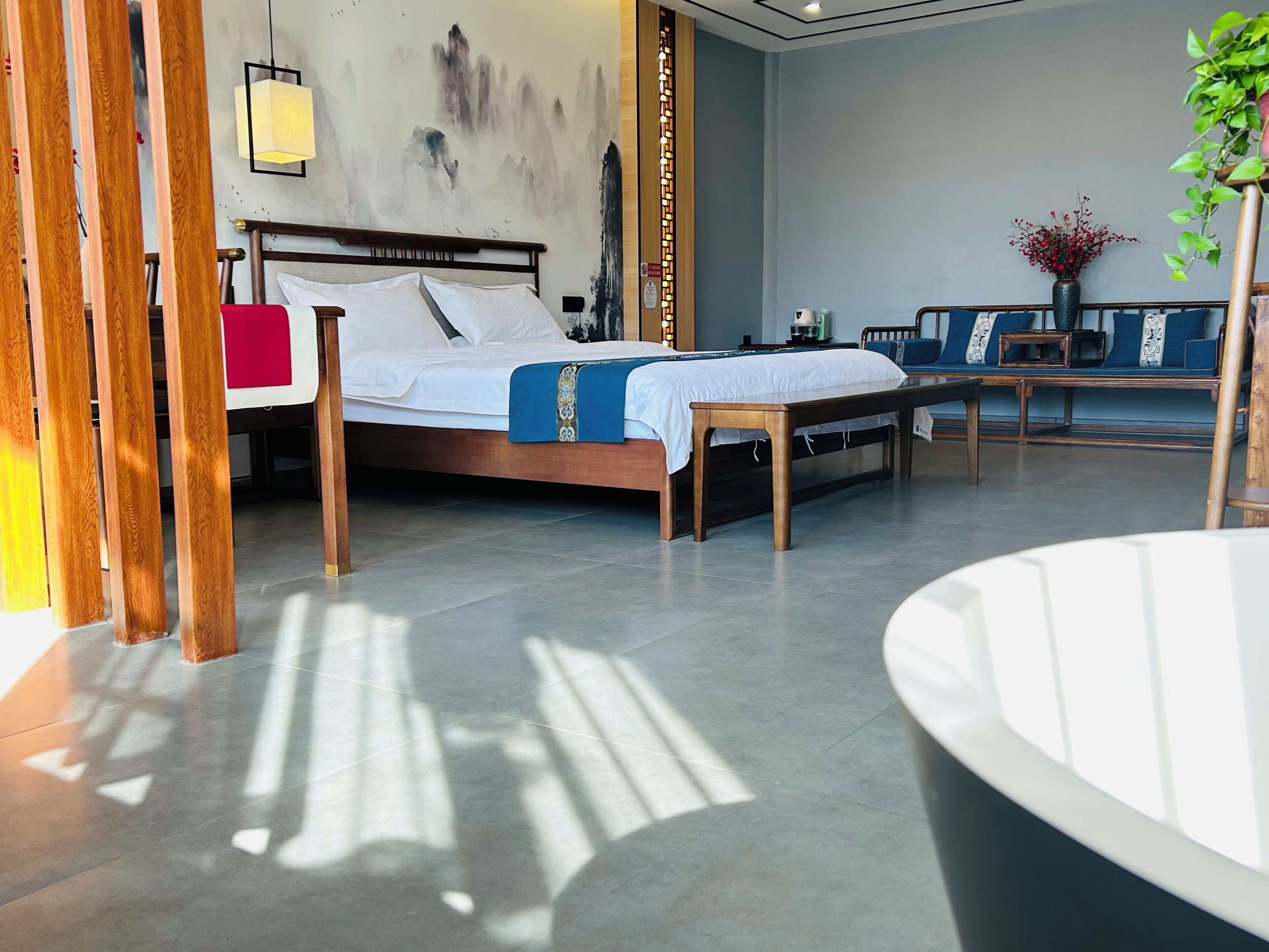 A modern hotel room with a large bed, a seating area with a bench, and a large window allowing natural light.