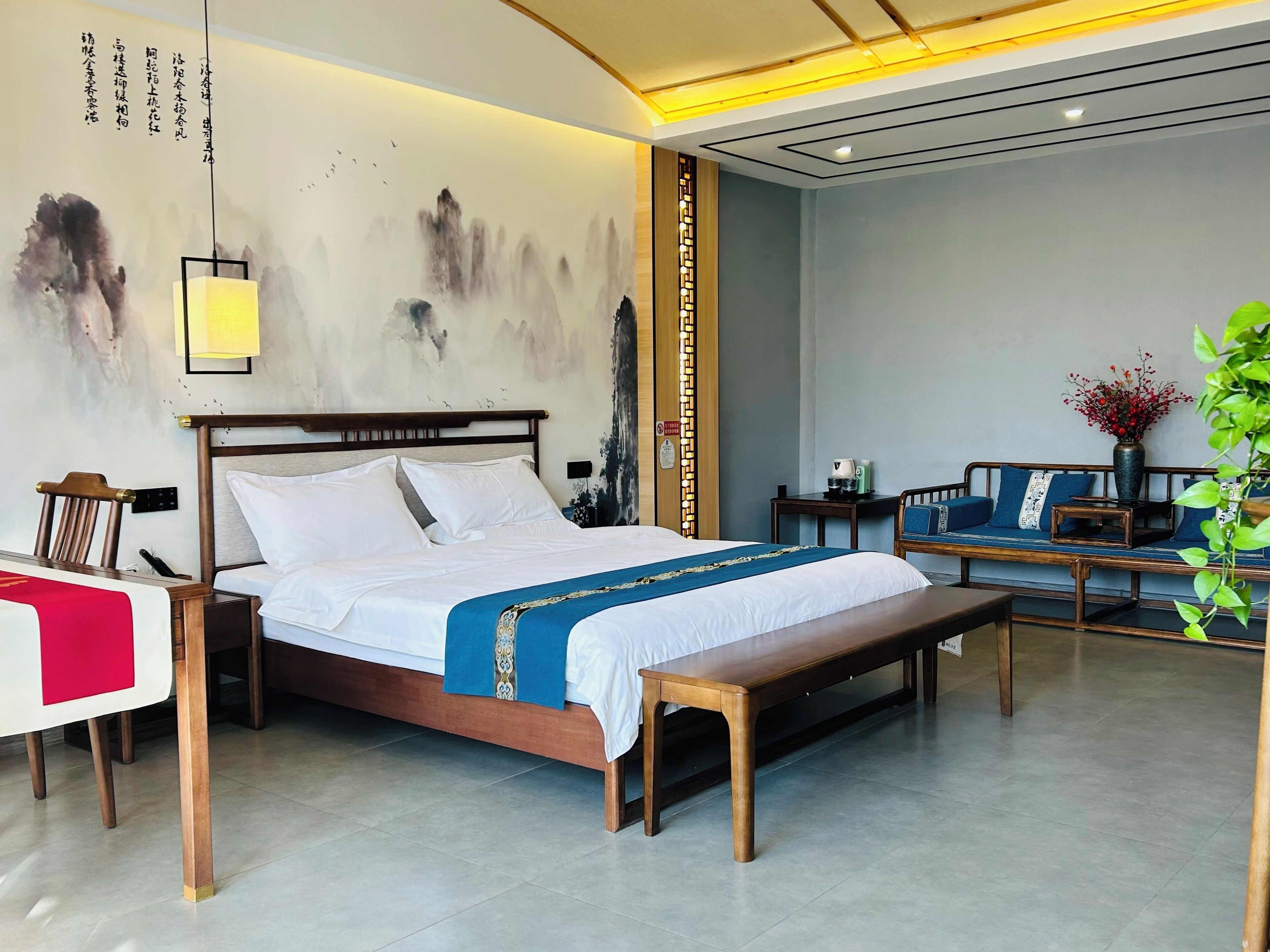 A hotel room with a bed, bedside tables, a bench, a sofa, and a wall with calligraphy.