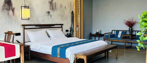 A hotel room with a bed, bedside tables, a bench, a sofa, and a wall with calligraphy.