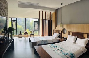 Una habitación de hotel moderna con dos camas, un ventanal que ofrece vistas a zonas verdes, un cabecero de madera y un banco empotrado.