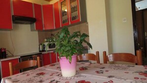 Un coin repas avec une table dressée pour quatre personnes, entouré d’armoires rouges et agrémenté d’un vase rose contenant une plante.