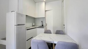 A compact kitchen with white cabinetry, a built-in refrigerator, a sink, and a marble-top dining table with four chairs. - One Bedroom Apartment with Terrace (Zaton)