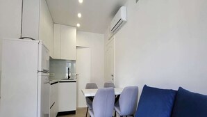 A compact kitchenette with a refrigerator, stove, and microwave. There is a dining table with four chairs and a blue couch in the foreground. - One Bedroom Apartment with Terrace (Zaton)