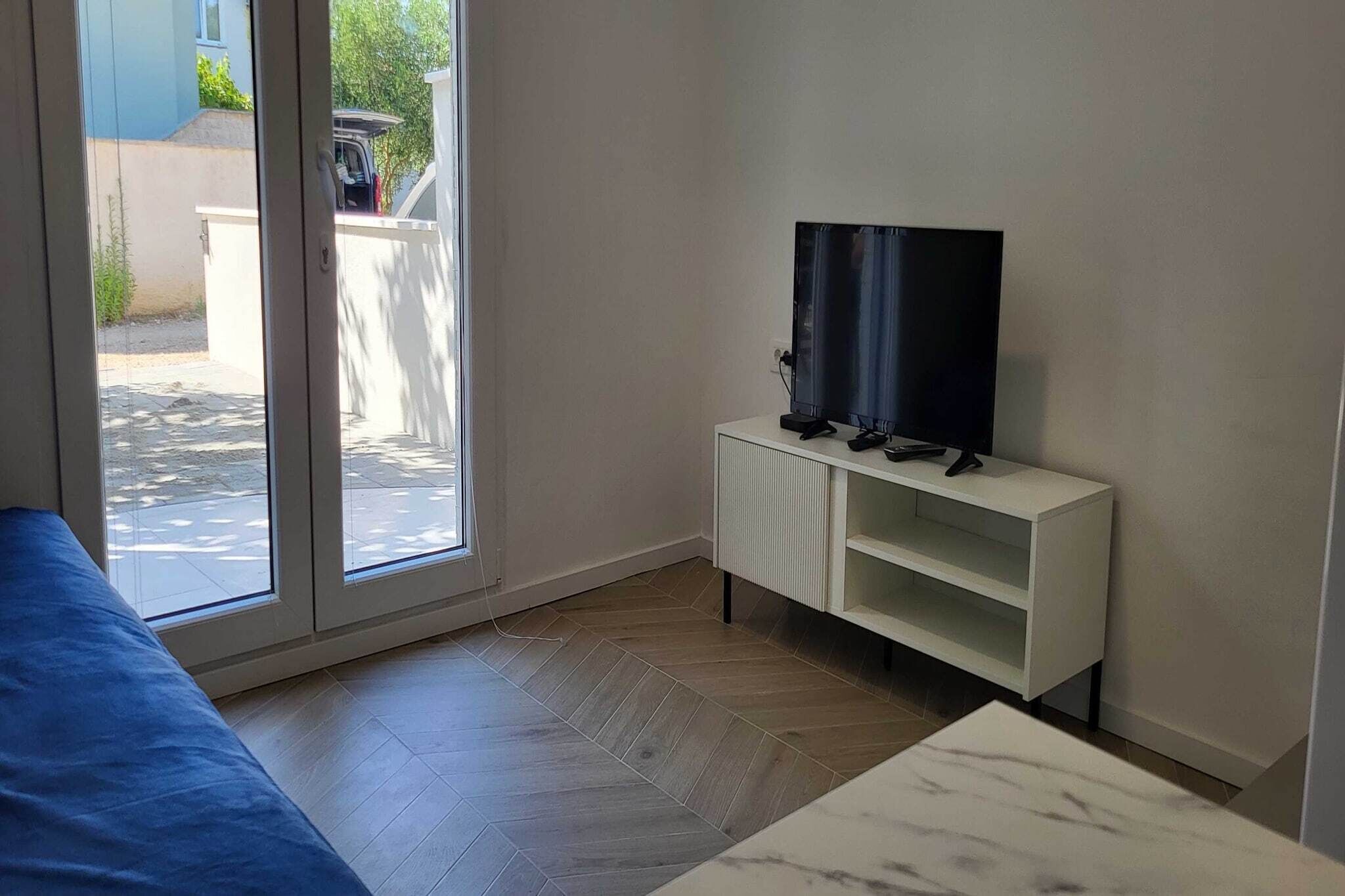 Una habitación con puerta de vidrio corrediza que da a un patio, un mueble blanco para televisor y un sofá azul.