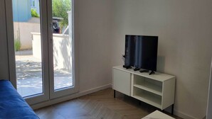 A room with a sliding glass door leading to a patio, a white TV stand, and a blue sofa. - One Bedroom Apartment with Terrace (Zaton)