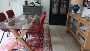 A dining area with a glass-top table, red chairs, a patterned rug, a cabinet with glass doors, and a lamp. - T3 apartment (two bedrooms) on garden level, garden 120 m2 town center, (Saint-Jean-de-Luz)