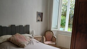A bedroom with a large bed, a chair, a nightstand, a picture on the wall, and a window with a view of greenery. - T3 apartment (two bedrooms) on garden level, garden 120 m2 town center, (Saint-Jean-de-Luz)