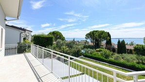 Ein Balkon mit weißer Brüstung, der auf einen Garten und ein Gewässer blickt.