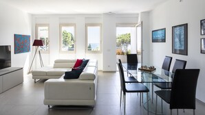 Ein modernes Wohnzimmer mit einer Couch, einem Esstisch mit Stühlen, einem Fernseher und Kunstwerken an den Wänden.