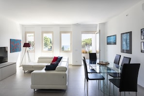 A modern living room with a sofa, a dining table with chairs, a TV, and artwork on the walls.