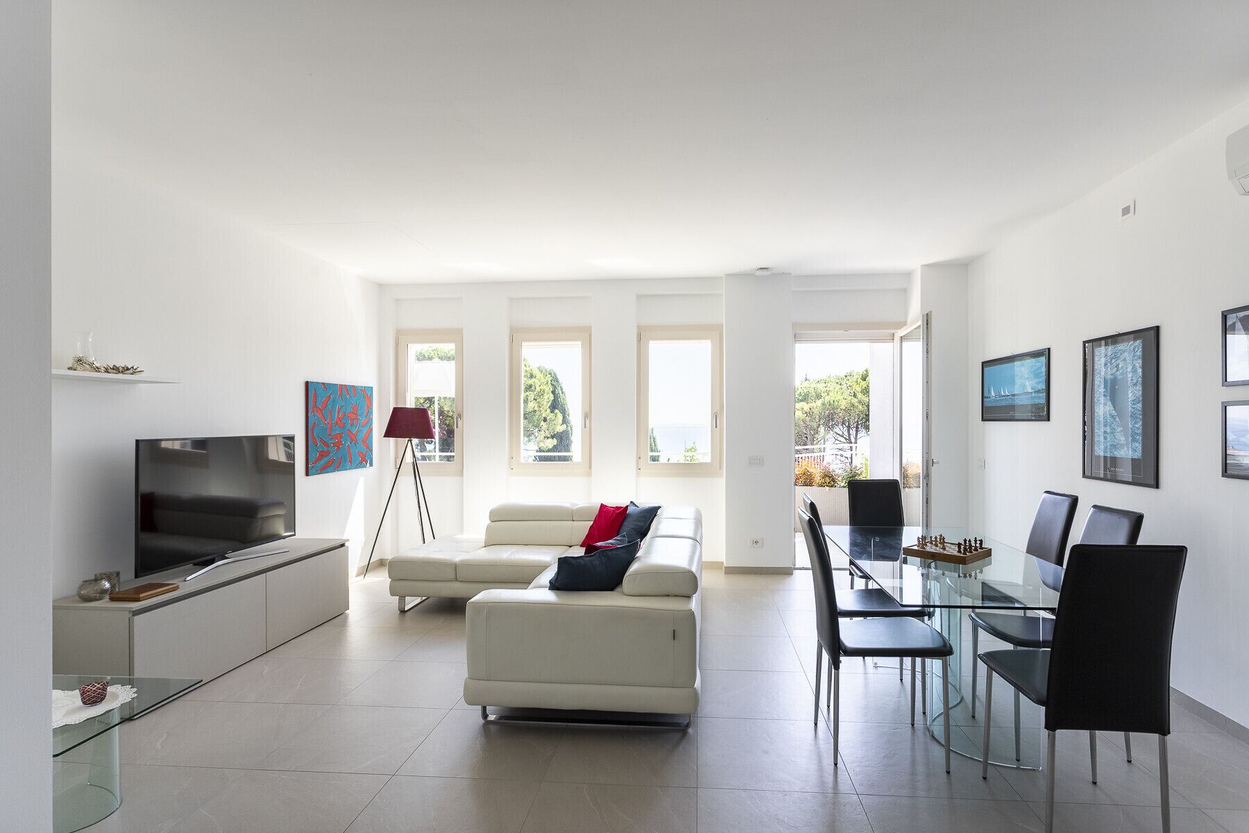 Una sala de estar moderna con televisor, sofá y comedor con sillas y una mesa de vidrio.