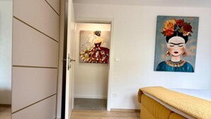 A room with a wooden floor, a yellow sofa, a painting on the wall, and a door leading to another room. - One-Bedroom Apartment With Terrace (Drace)