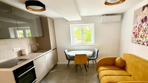 A modern kitchen with a dining area, a sofa, and a window with a view of greenery. - One-Bedroom Apartment With Terrace (Drace)