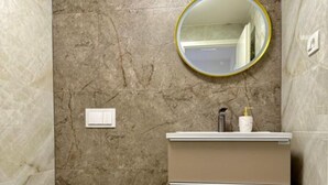 A bathroom with a marble wall, a round mirror, a white sink, and a bottle of soap. - One-Bedroom Apartment With Terrace (Drace)