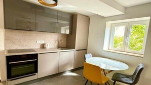 A modern kitchen with a built-in oven, a dining table with chairs, and a window with a view of greenery. - One-Bedroom Apartment With Terrace (Drace)