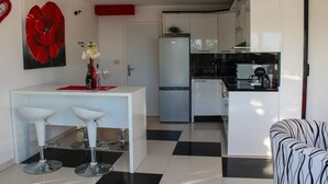 A modern kitchen with white cabinets, a black countertop, and a refrigerator. There is a white bar area with two stools and a vase with flowers. - Two Bedroom Apartment with Sea View and Private Pool (Pisak)