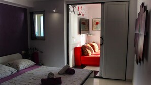 A bedroom with a bed, a red sofa, and a door leading to another room. - Two Bedroom Apartment with Sea View and Private Pool (Pisak)