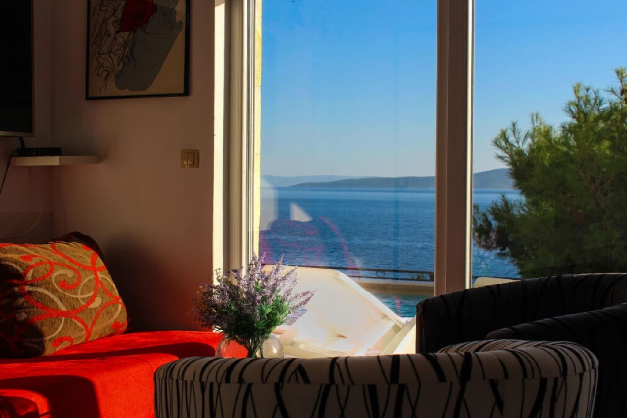 Una habitación con un ventanal grande que da a una masa de agua, un sofá rojo y un cojín estampado.