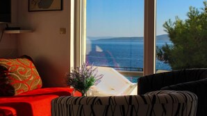 A room with a large window overlooking a body of water, a red sofa, and a patterned cushion. - Two Bedroom Apartment with Sea View and Private Pool (Pisak)