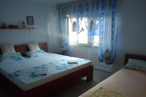 Une chambre à coucher comprenant un lit, une table de chevet, une fenêtre avec des rideaux et une étagère fixée au mur, sur laquelle sont posés divers objets.