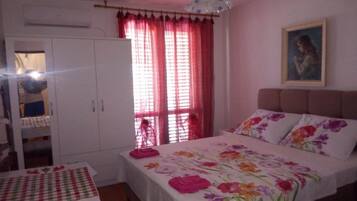 A bedroom with a bed, a wardrobe, a window with curtains, and a painting on the wall.