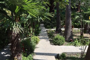 A stone pathway flanked by lush greenery and palm trees, leading through a garden area. - Silver Gate Rooms-Diocletian's Palace - Quardruple Room 1 (Split)