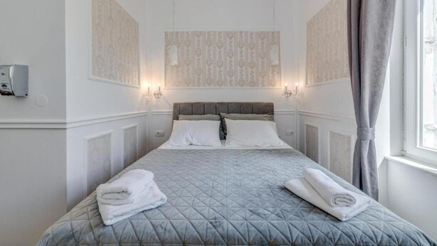 Habitación de hotel con cama, dos apliques en la pared, una ventana con cortinas y un termostato en la pared.