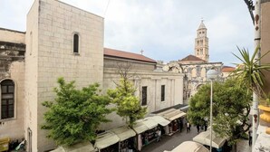 Una calle con un edificio que tiene un ventanal pequeño y un árbol delante.