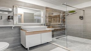 Un baño moderno con cabina de ducha de vidrio, un espejo grande y un lavamanos blanco.