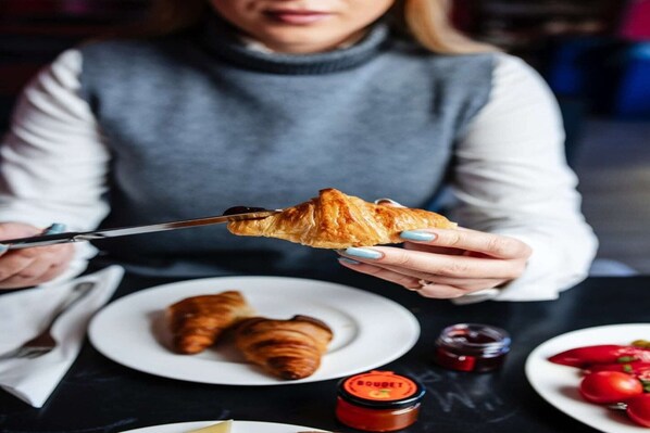 A person holding a croissant with a knife, with two croissants on a plate and a jar of jam on the table. - Silver Gate Rooms-Diocletian's Palace - Six-Bed Room (Split)