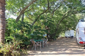 Un espacio comedor al aire libre cubierto, con una mesa y sillas, rodeado de árboles y follaje.
