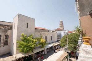Una plaza urbana histórica con una torre destacada al fondo, rodeada de edificios tradicionales y puestos de mercado.