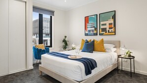 Une chambre moderne avec un grand lit, une table de chevet avec une lampe, une chaise et deux tableaux encadrés accrochés au mur.