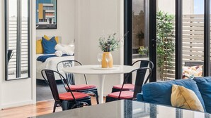 Une chambre moderne avec un lit, une table à manger et des chaises, un vase de fleurs et une grande fenêtre.