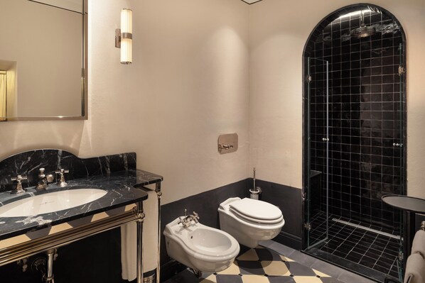 Une salle de bain moderne avec un sol à carreaux noirs et blancs, un lavabo blanc doté d’un plan de toilette en marbre, un bidet et une douche à l’italienne avec des carreaux noirs.