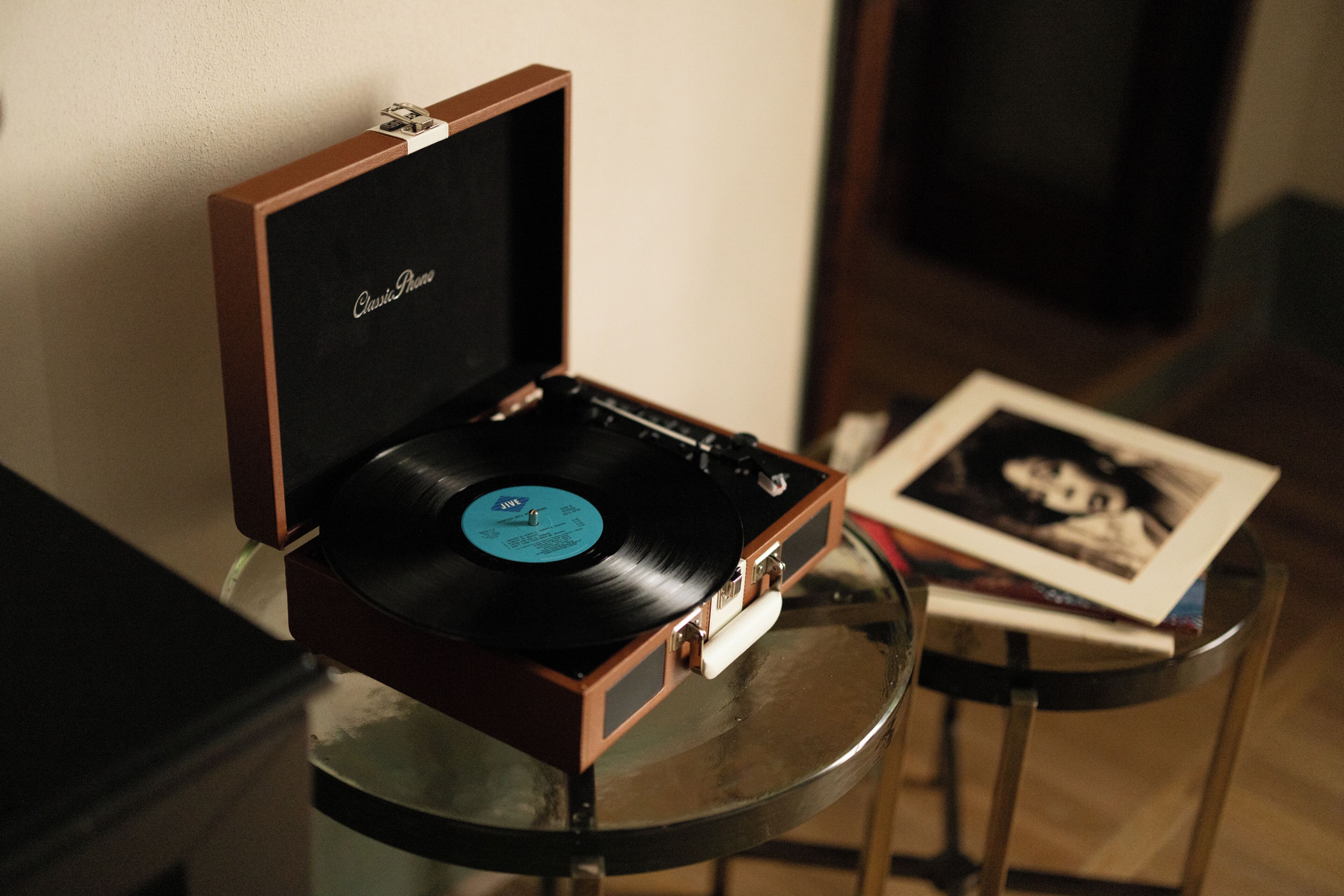 Um disco de vinil numa caixa de madeira sobre uma mesa de vidro, com uma fotografia ao lado.