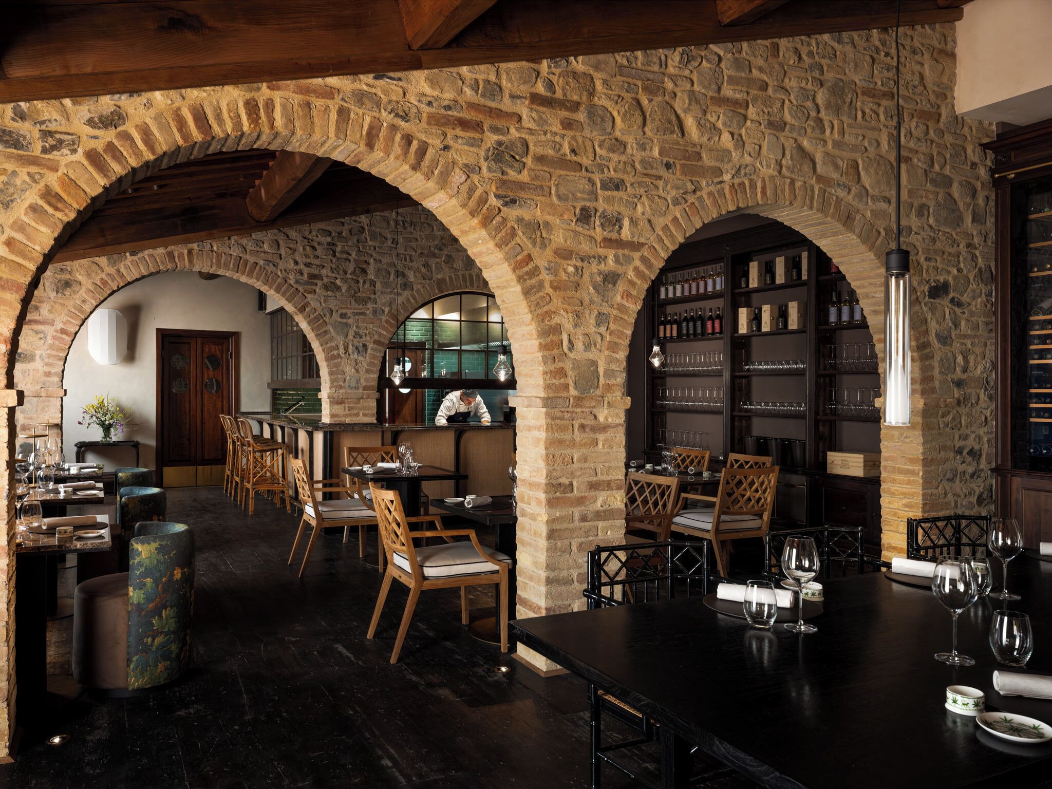 Un intérieur rustique avec des arches en pierre, des meubles en bois et un coin bar agrémenté de verres à vin.