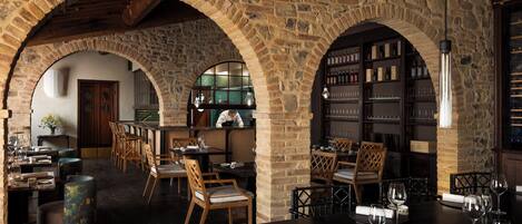 A rustic interior with stone arches, wooden furniture, and a bar area with wine glasses.