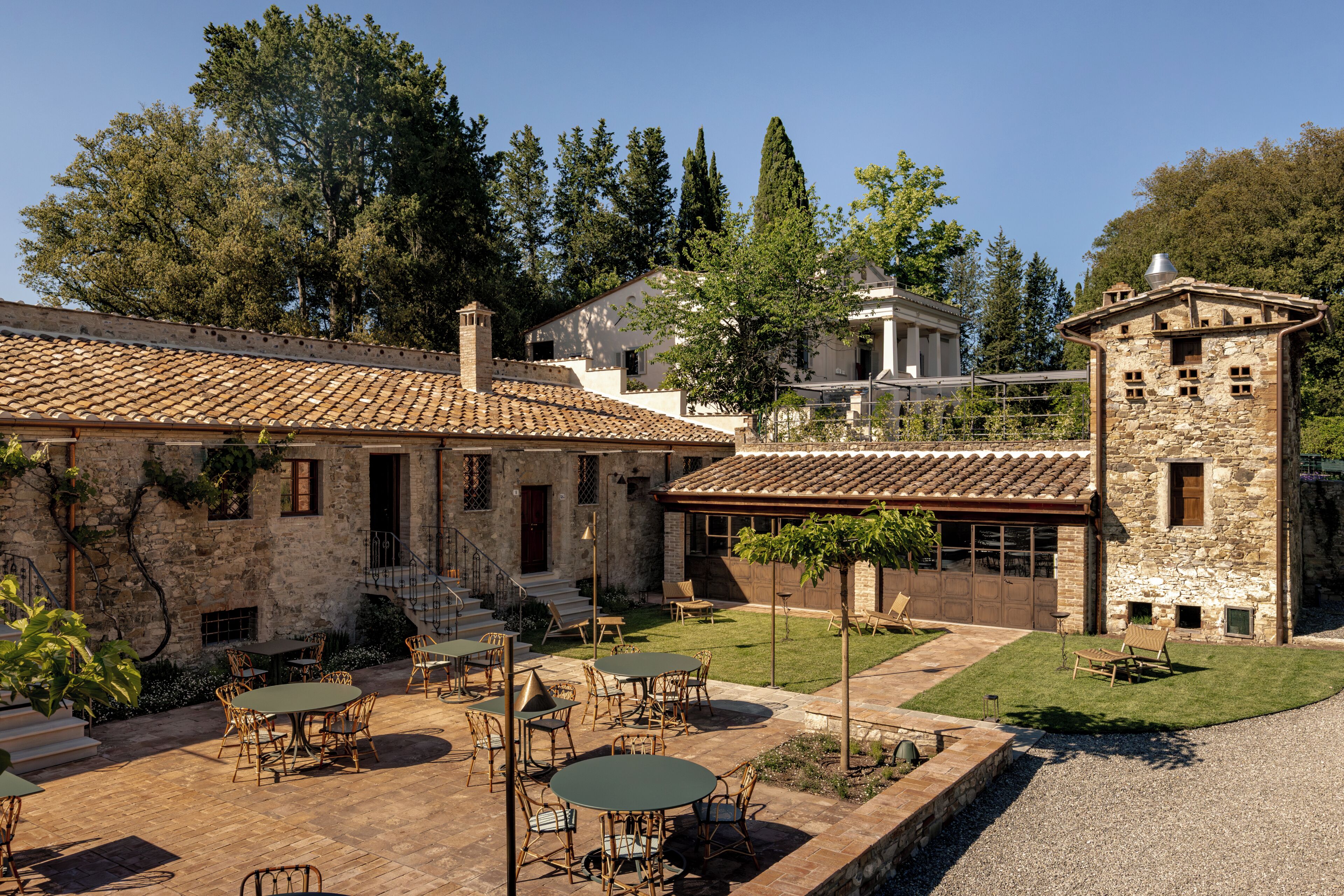 A courtyard with outdoor seating, stone buildings, and a clear sky.