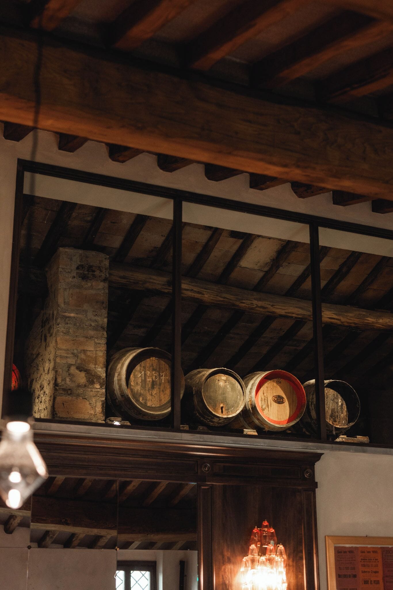 A room with wooden beams, a brick wall, and wooden barrels on a shelf.