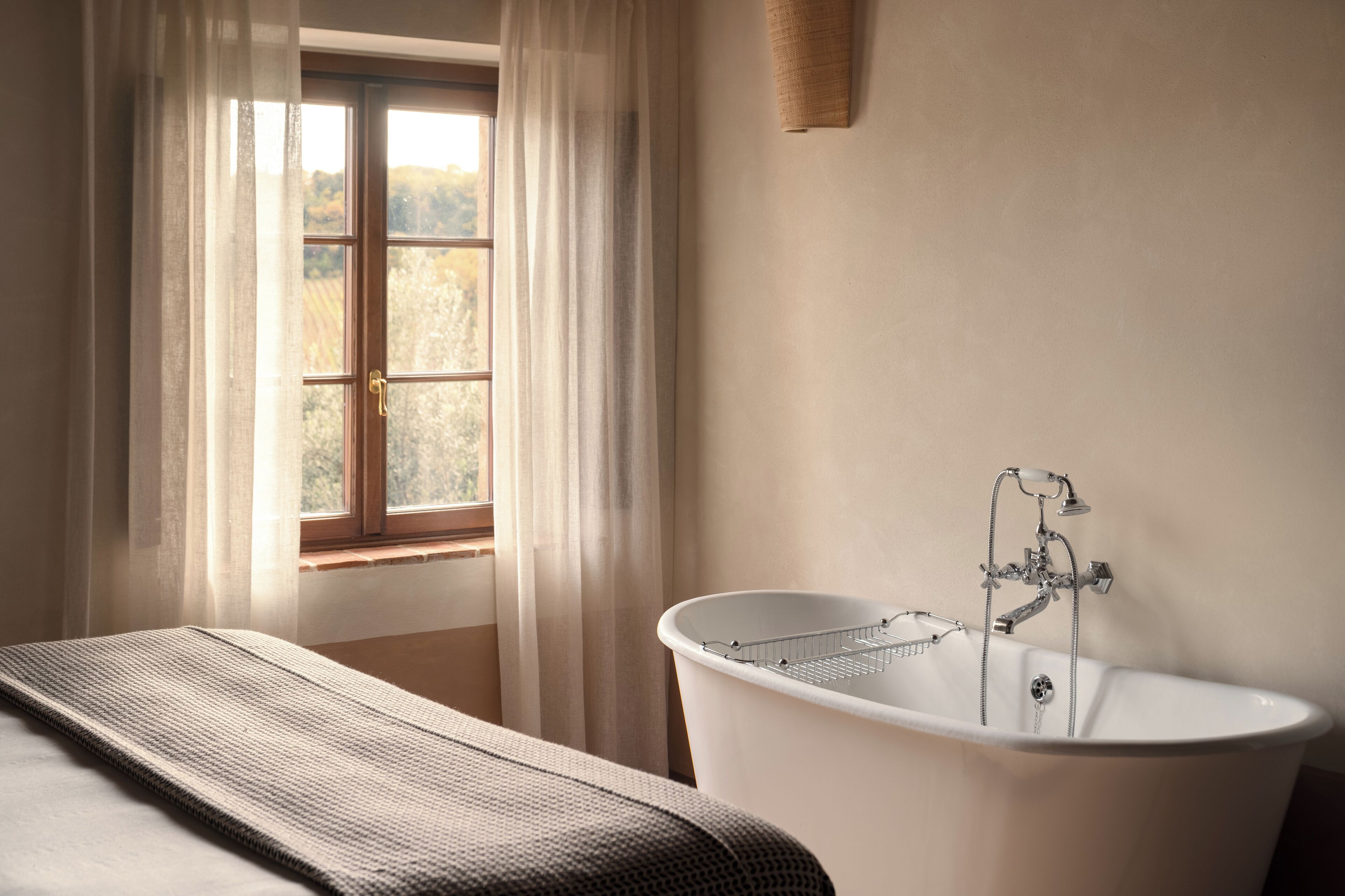 A bathroom with a freestanding bathtub, a window with curtains, and a towel on the floor.