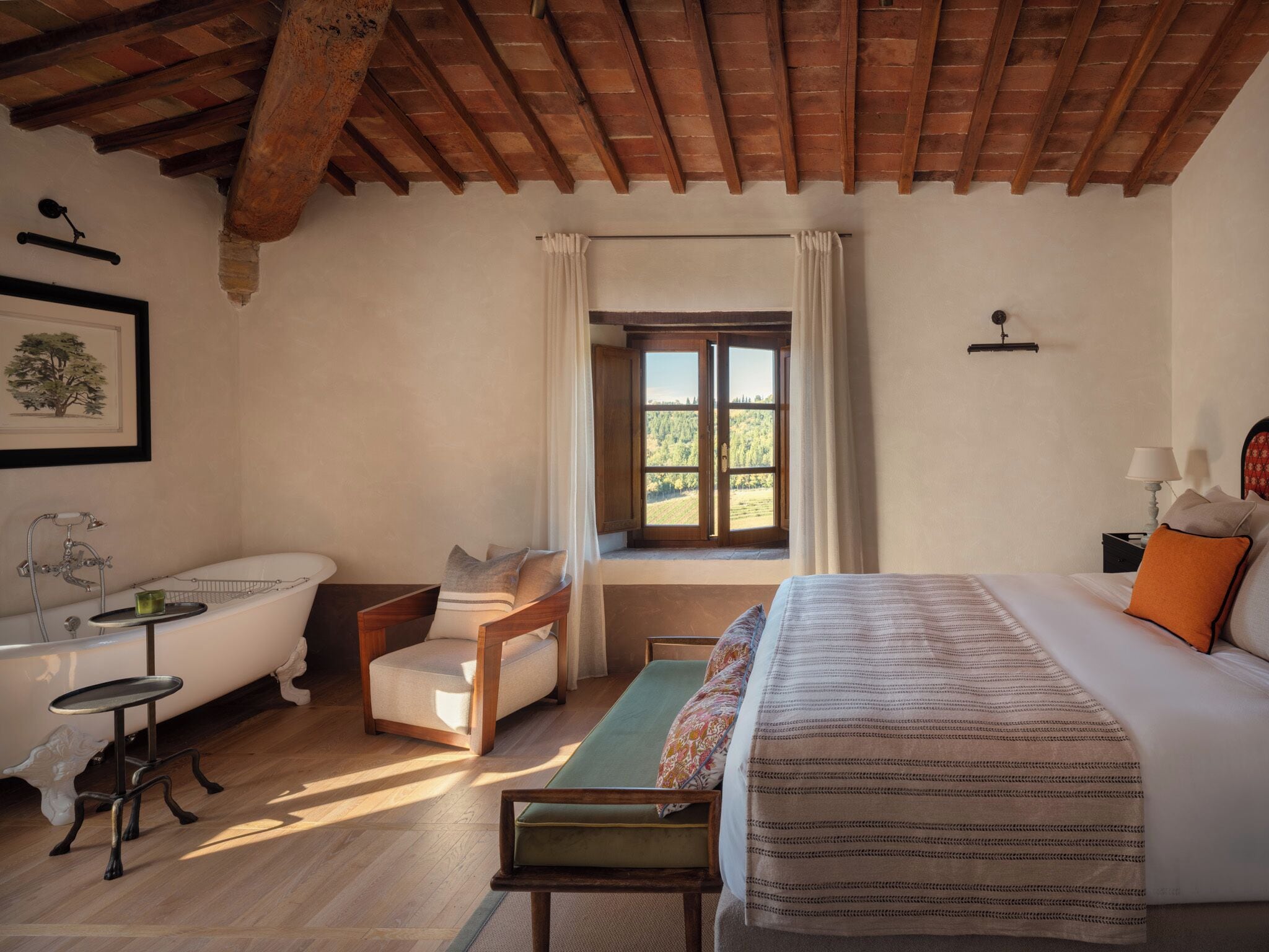 A bedroom with a large bed, a wooden chair, a small table, a bathtub, and a window with curtains.