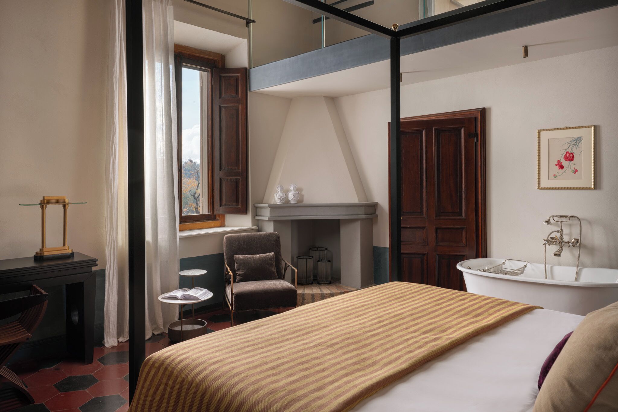 A hotel room with a bed, a chair, a small table, a fireplace, and a bathtub.