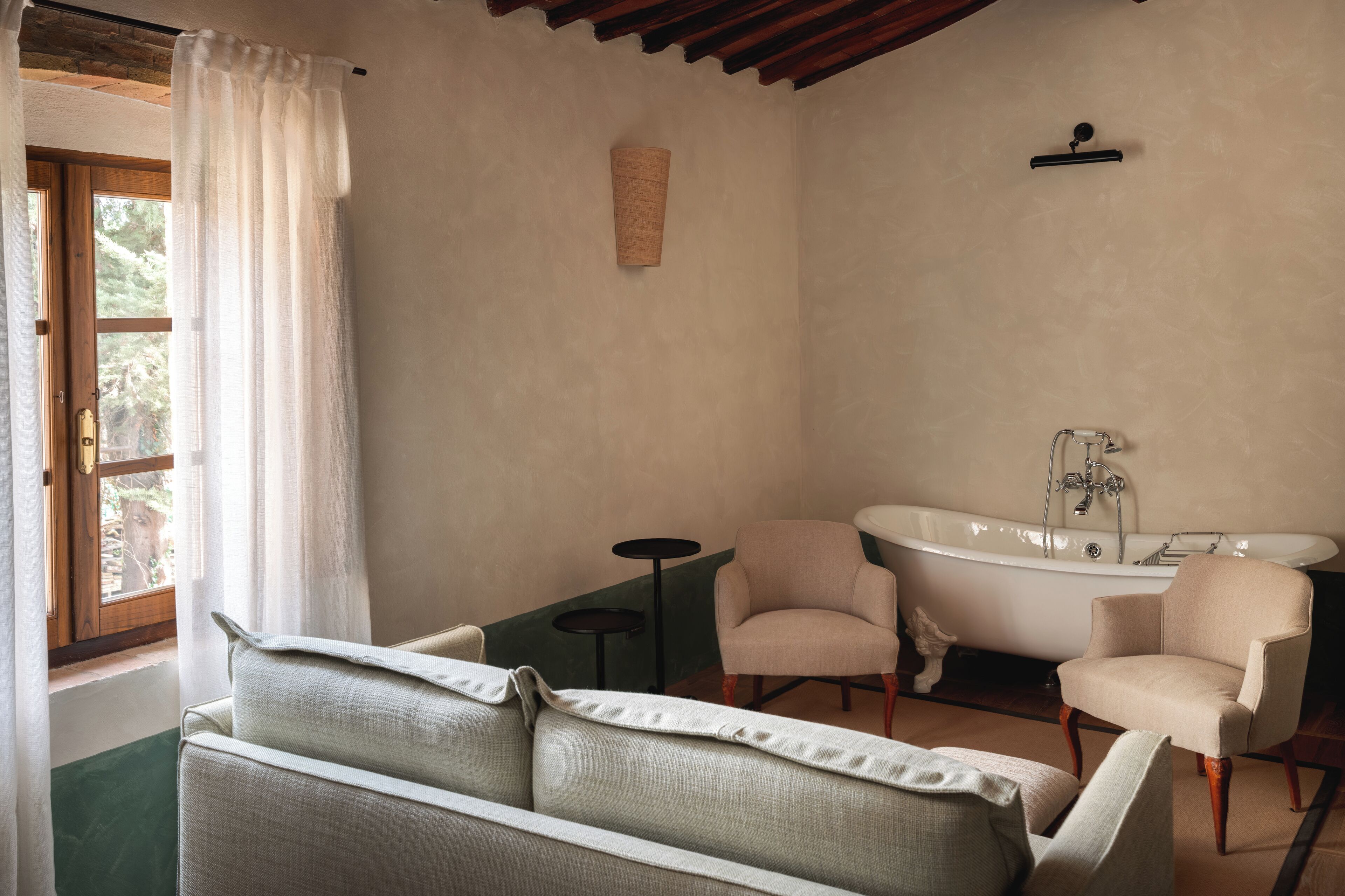 Un baño con bañera, dos sillones, una mesita y una ventana con cortina.
