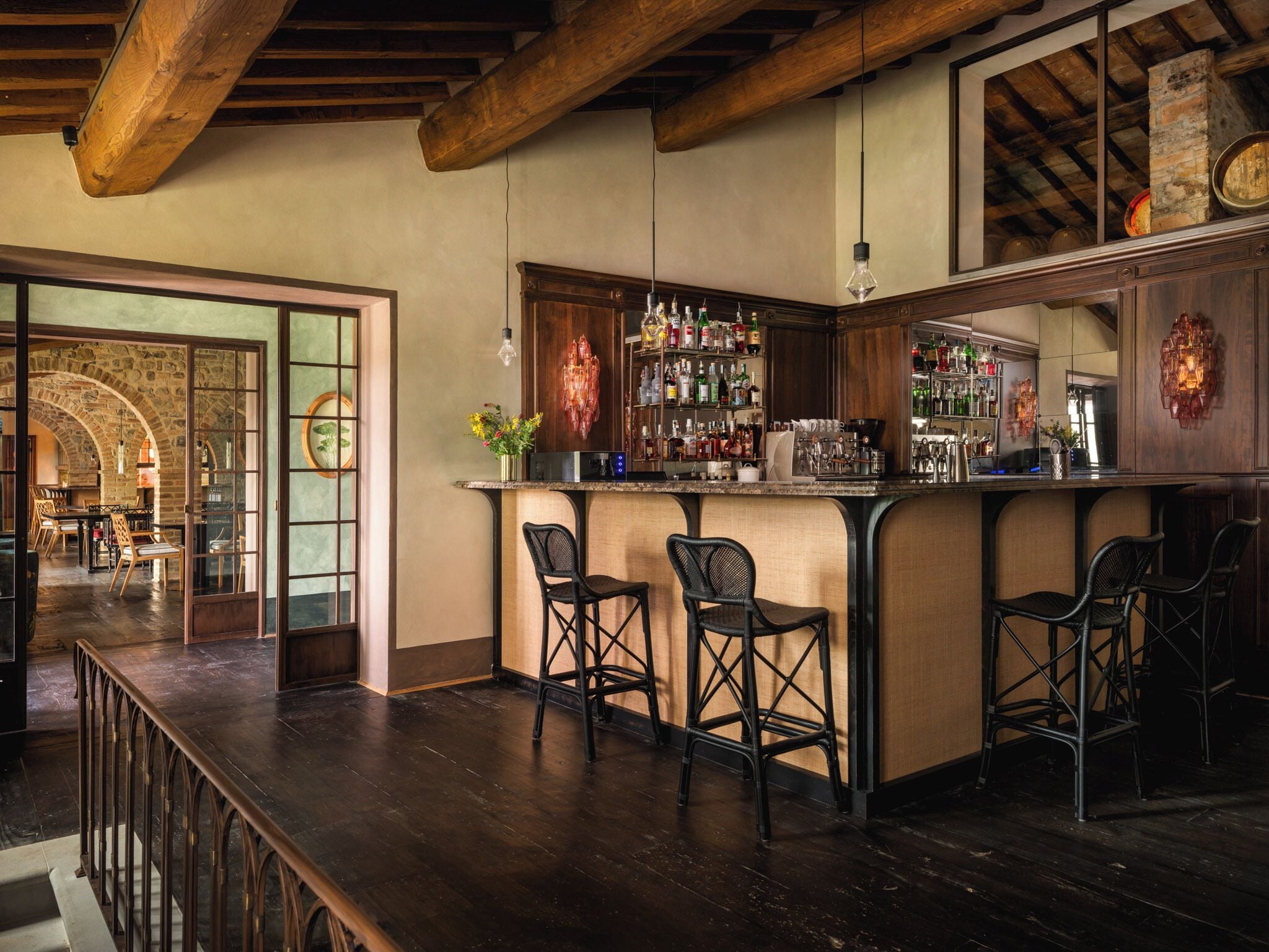 Un espace bar agrémenté de poutres en bois, d’une arche en pierre et d’un comptoir avec des tabourets.