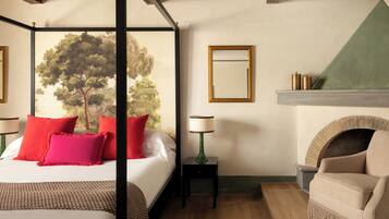 A bedroom with a four-poster bed, a fireplace, a green lamp, and a view of trees through the window.